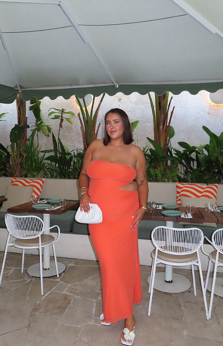Full length view of an orange strapless maxi dress with side waist cutouts and a fitted silhouette