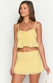 Close-up of the ruched waist and layered sheer fabric of a yellow mini skirt