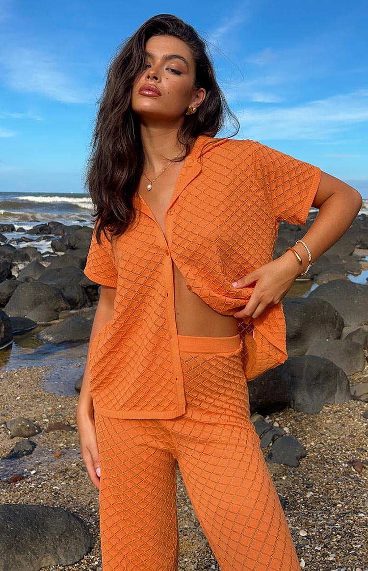 Close-up of the orange knit top's diamond pattern and open front, with matching knit pants visible