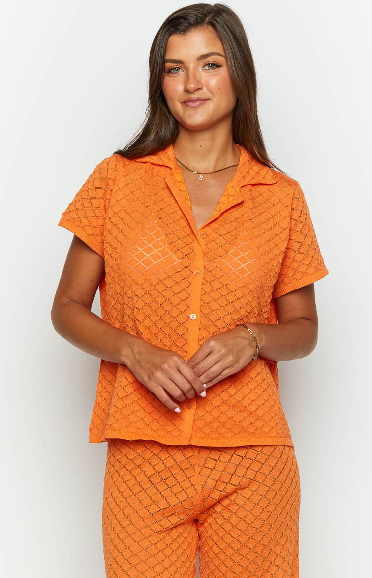 Front view of an orange knit top with a collared neckline, short sleeves, and a button-front placket, showing the diamond open-knit texture