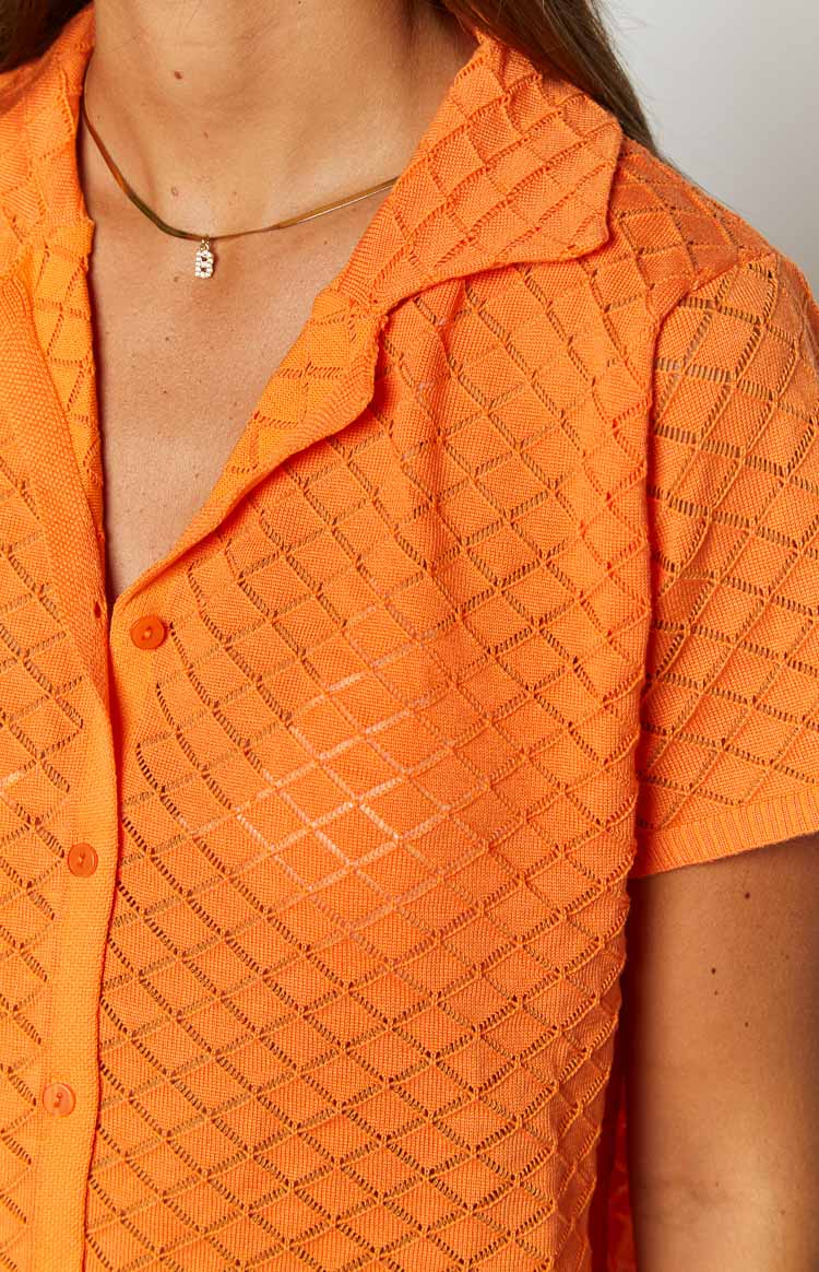Close-up of the orange knit top's diamond open-knit pattern, pointed collar, and button placket