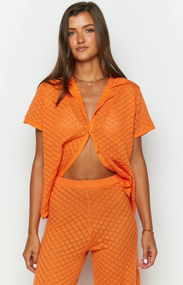 Orange collared knit top with short sleeves, unbuttoned front revealing the midriff, and matching diamond knit pants