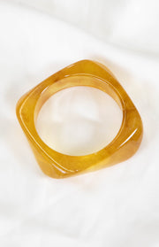 Angled view of a translucent yellow resin square bangle with marbled amber tones and rounded corners