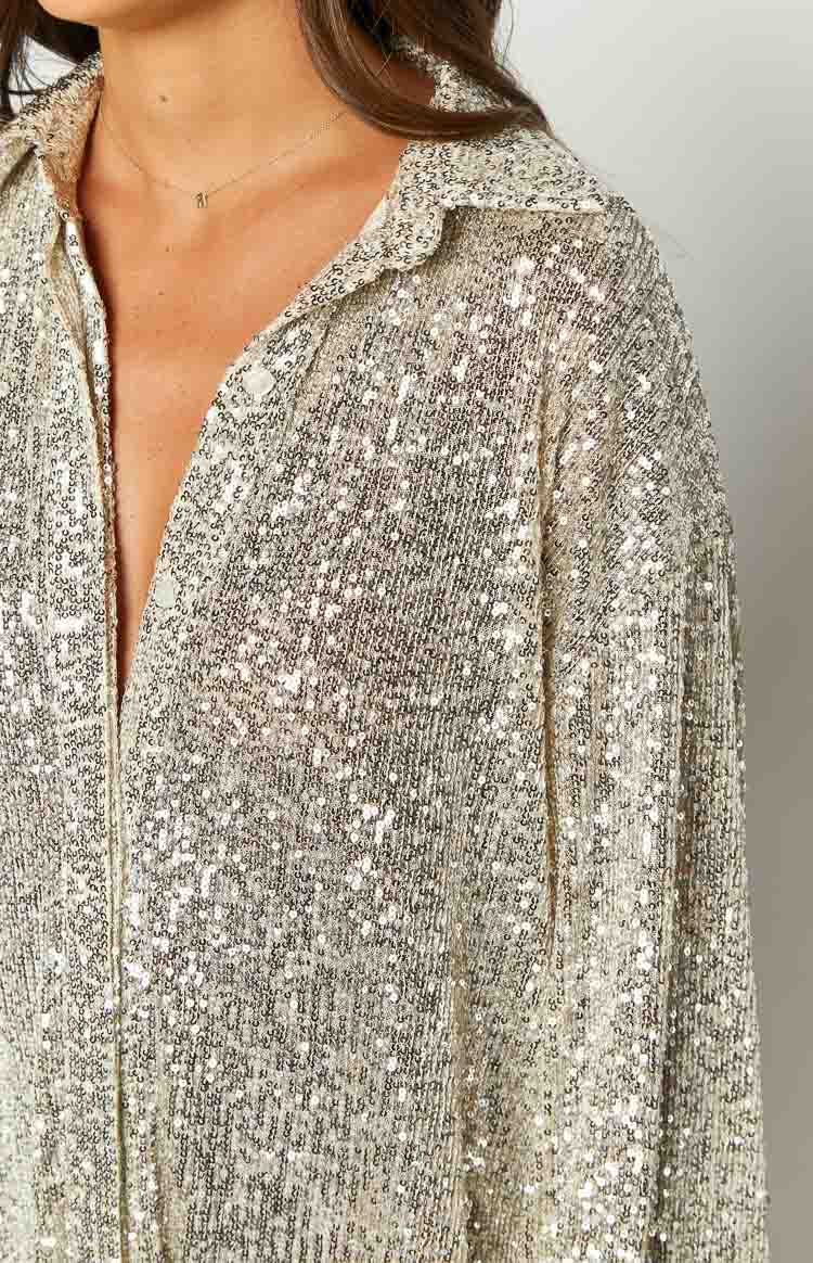Close-up of the gold sequin fabric, collared neckline, and button-front detail of the long sleeve shirt