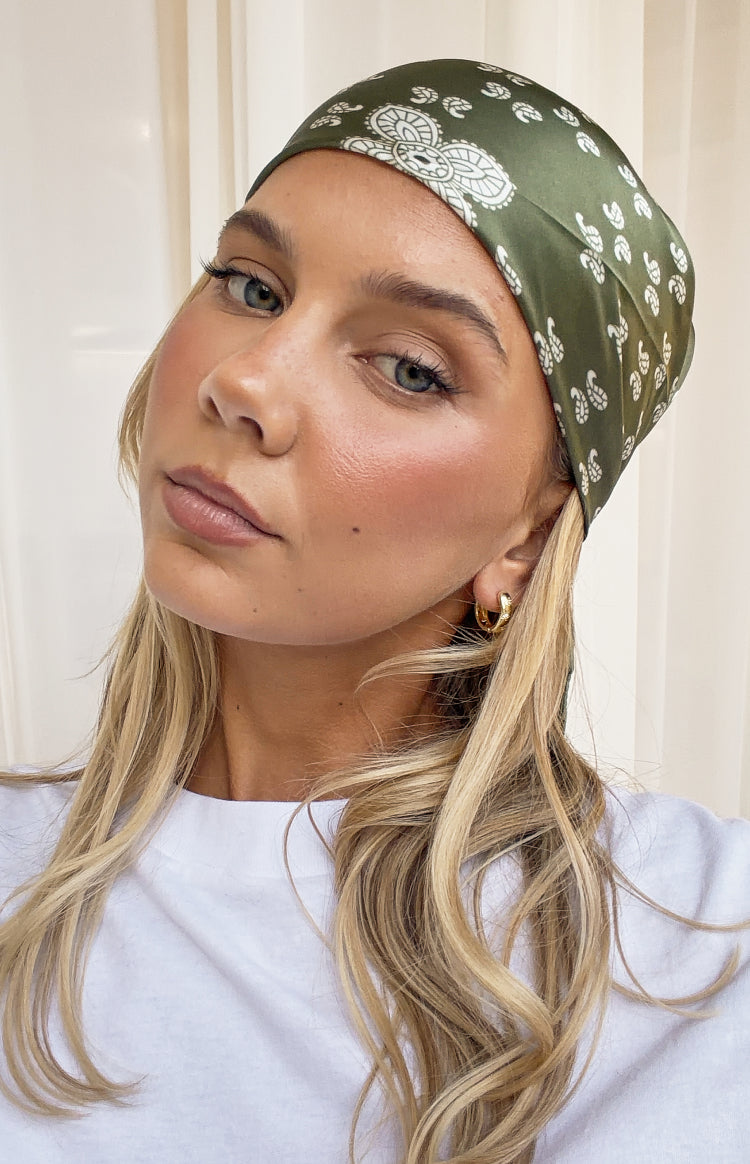 Close-up of a green satin triangle scarf with white paisley print worn as a headscarf