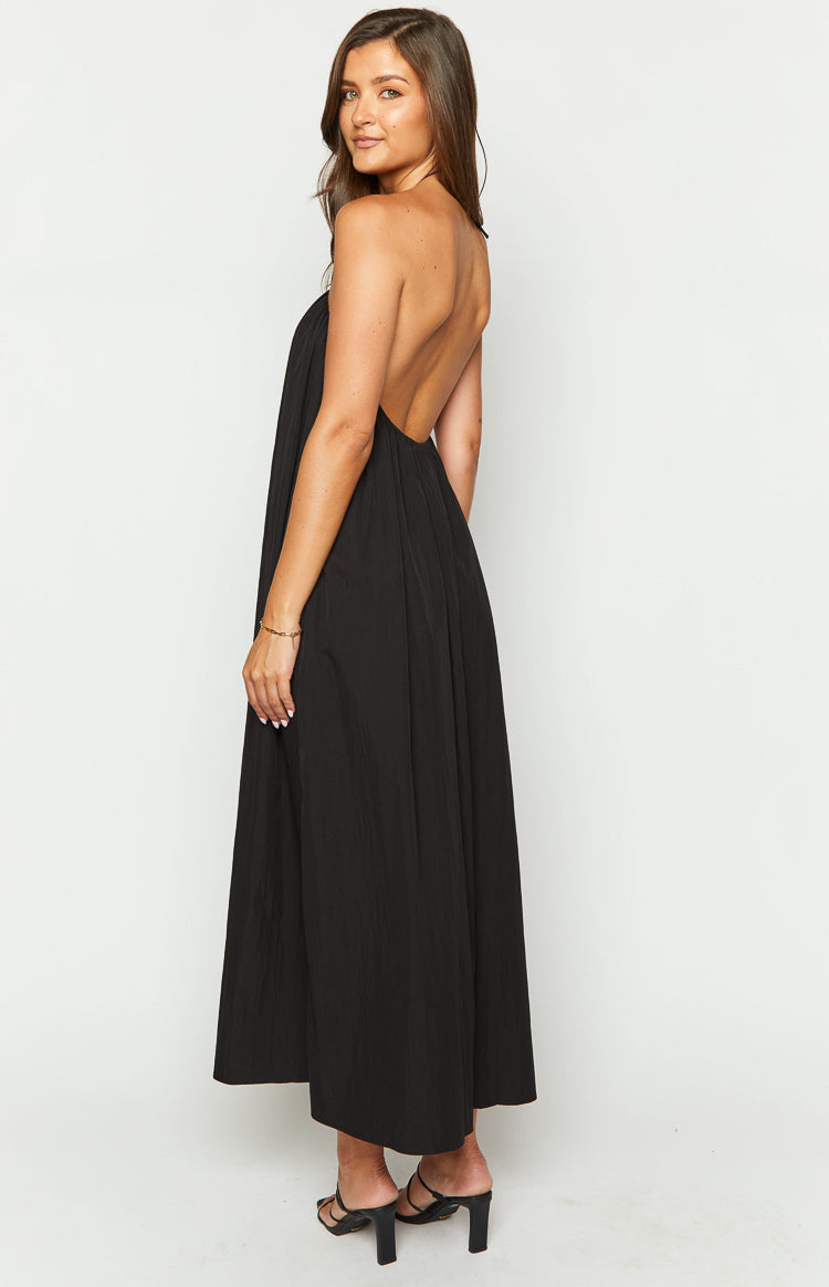 Side view of a black halter neck maxi dress with a low open back and flowy crinkled skirt