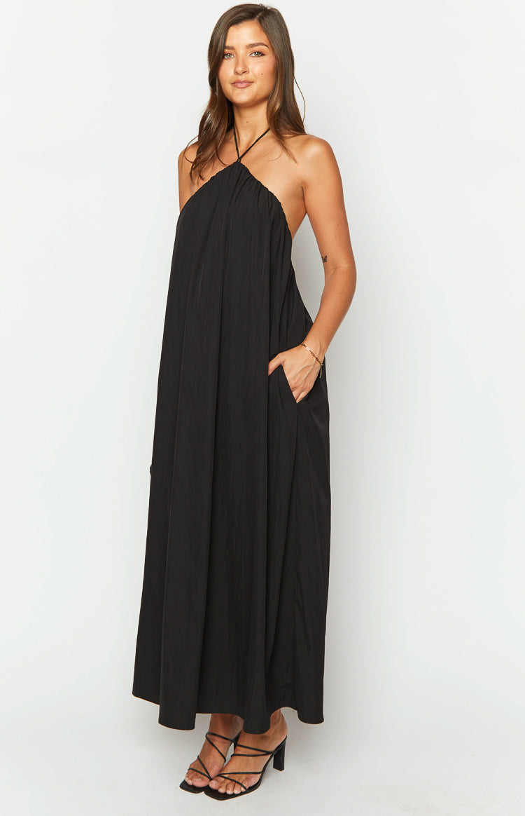 Side view of a black crinkled halter neck maxi dress with a loose, flowy silhouette and side pockets