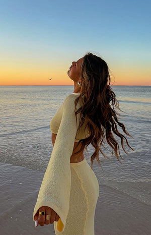Side view of a yellow knit maxi dress with long wide sleeves, textured fabric, and a midriff cut-out