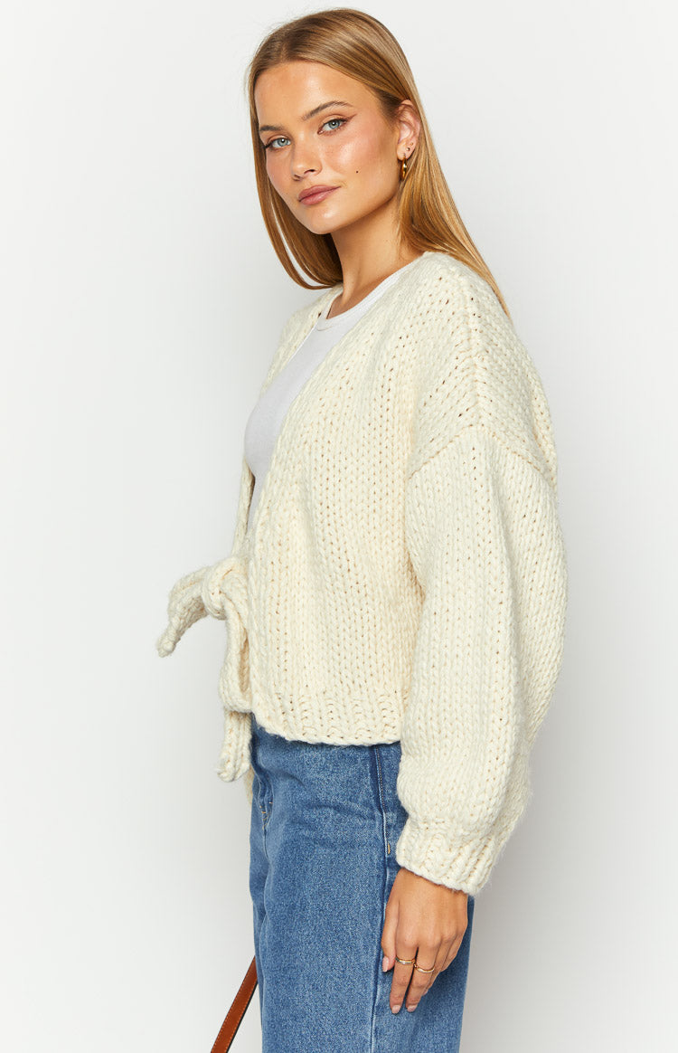 Side view of a cream chunky knit cardigan with a prominent side tie closure and relaxed long sleeves