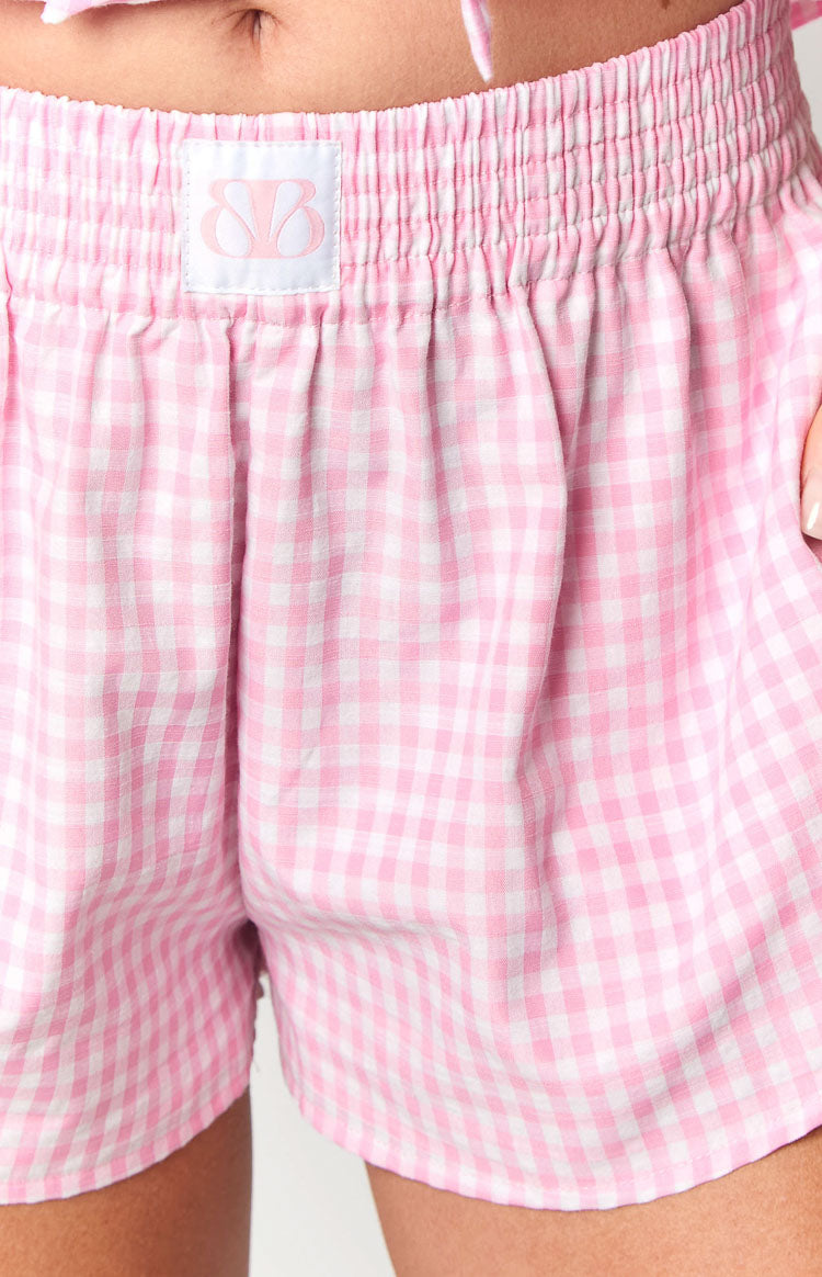 Close-up of the elasticated waistband on pink gingham shorts with a white logo label