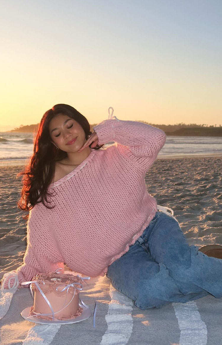 Off-shoulder baby pink chunky knit sweater with white tie details on the shoulders and a relaxed fit