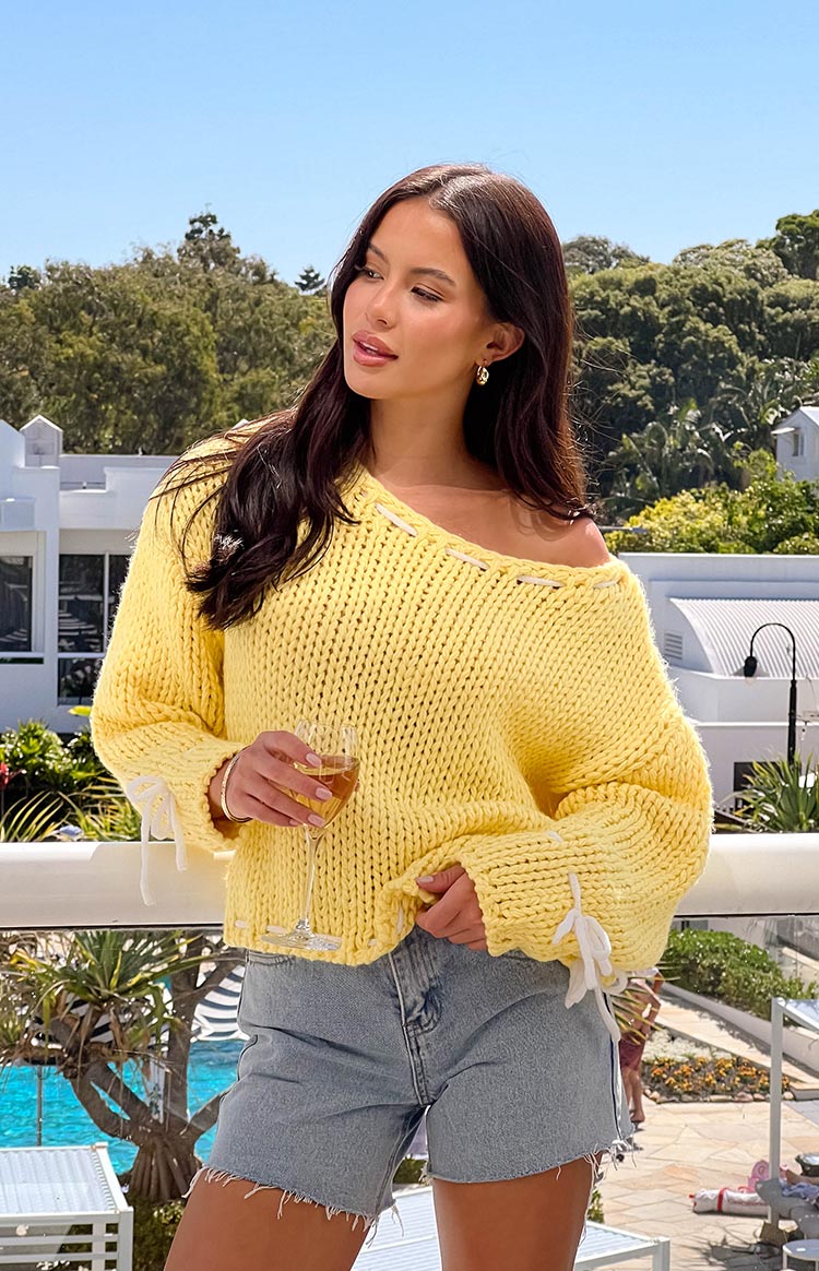 Yellow chunky knit sweater with white lacing detail along the off-shoulder neckline and cuffs