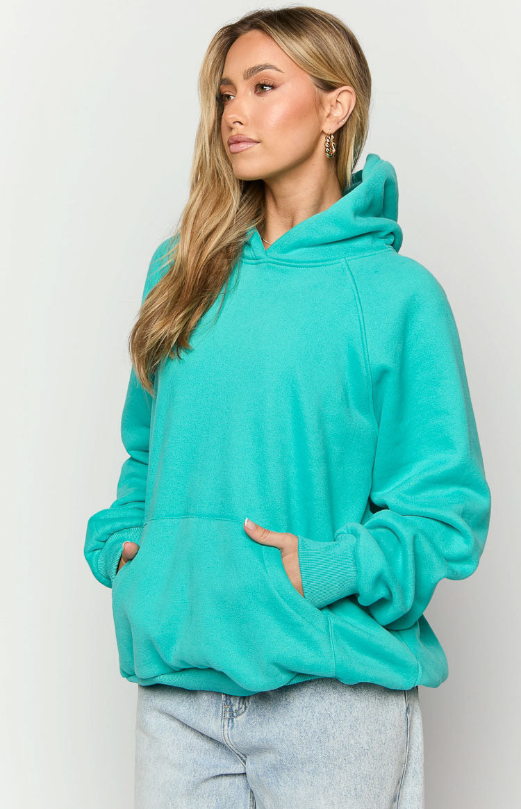 Close-up of the front kangaroo pocket and raglan sleeves on a teal oversized hoodie