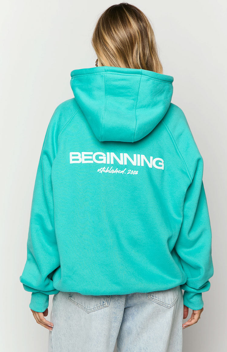 Rear view of a teal oversized hoodie with white 'BEGINNING established. 2008' text on the back