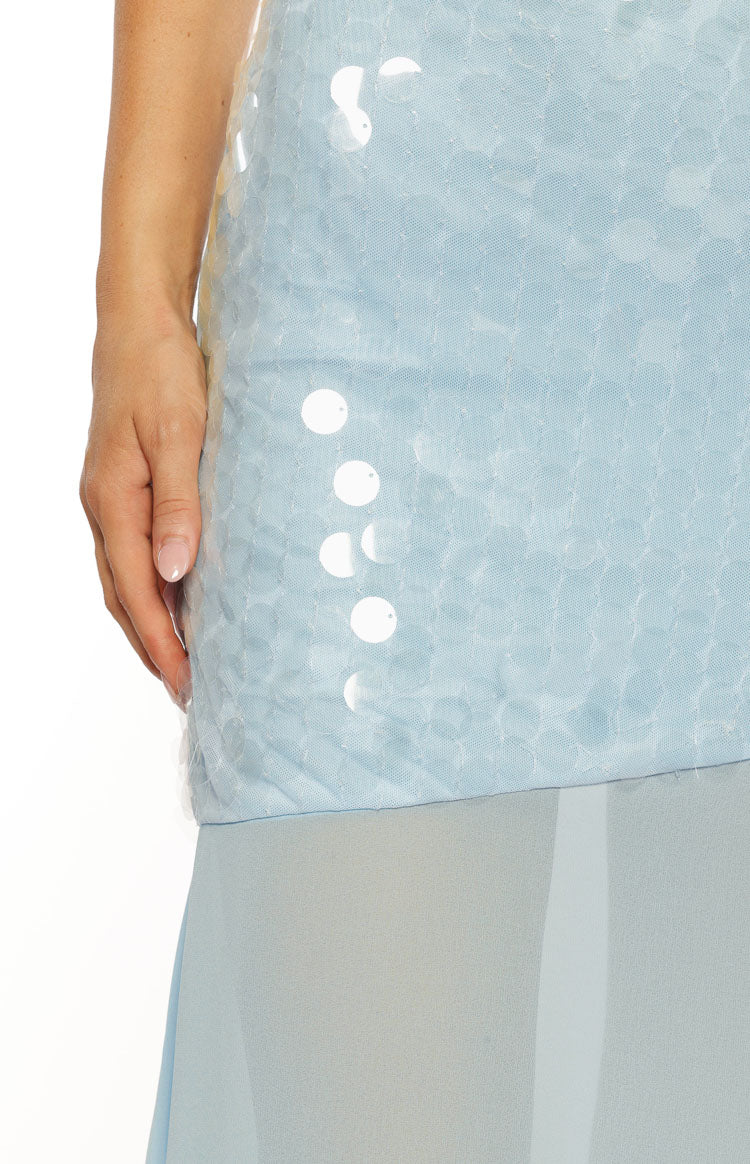 A very close up detail shot of the lower portion of the sequined bodice and the transition to the sheer skirt of a light blue dress. The image highlights the texture of the light blue fabric underneath large circular white iridescent sequins.