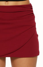 Close-up of the ruched side and wrap front detail on a burgundy mini skirt