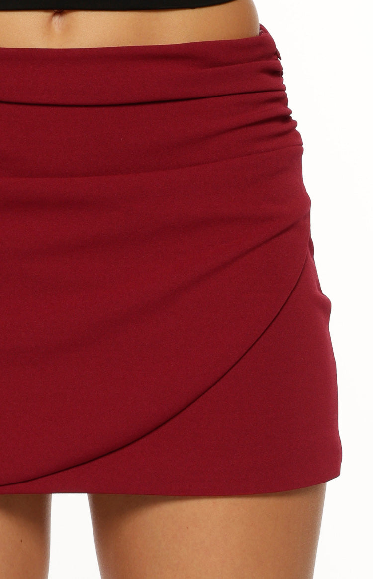 Close-up of the ruched side and wrap front detail on a burgundy mini skirt