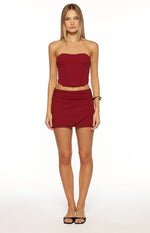 Front view of a burgundy wrap mini skirt with a ruched waist and an asymmetrical hem
