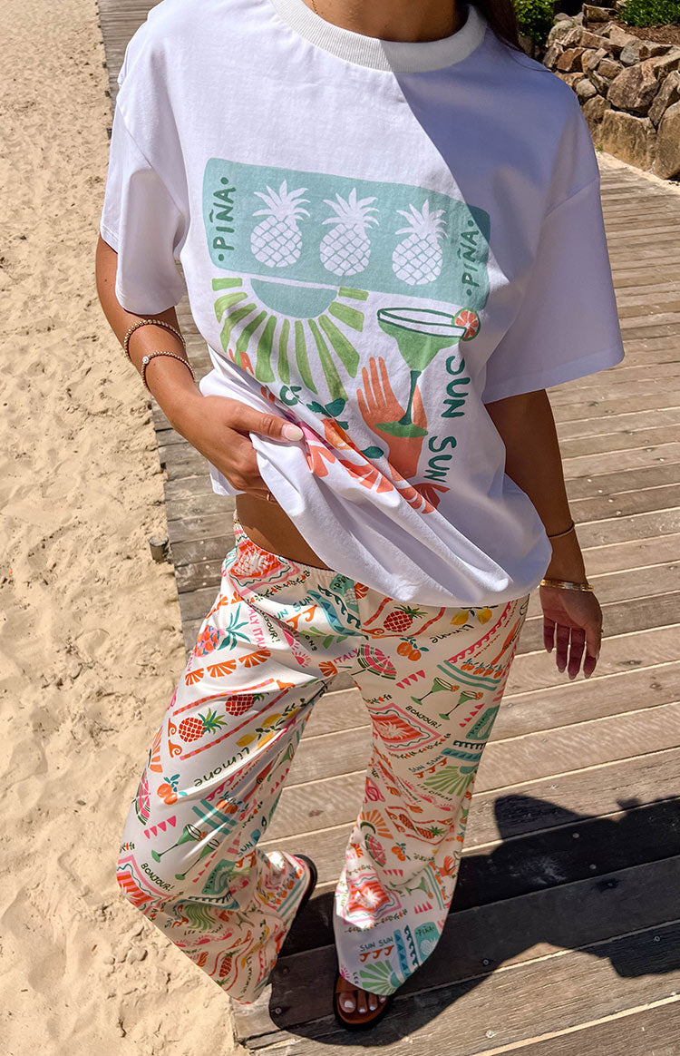 White wide-leg pants with a colourful Dolce Vita print featuring pineapples, cocktails, and lemons