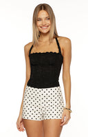 A close-up shot of our model wearing a pair of high-waisted shorts in a white fabric patterned with black polka dots. These shorts have a simple tailored cut.