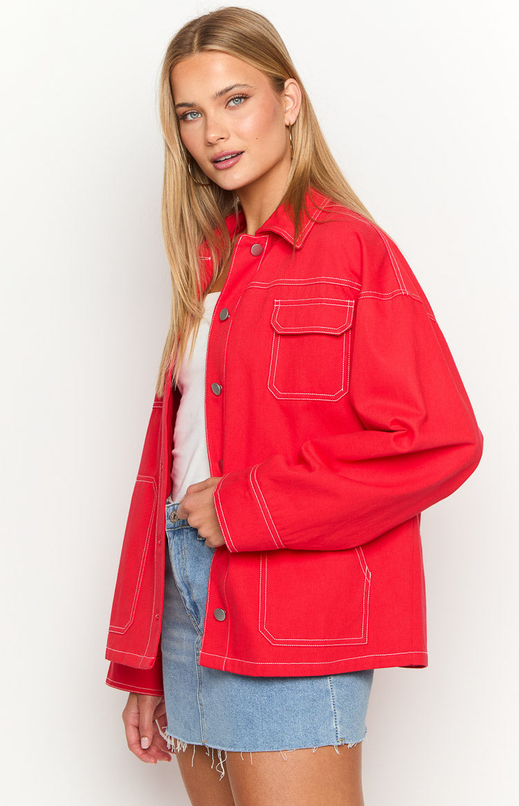 Angled front view of a red denim jacket with white contrast stitching and flap chest pockets