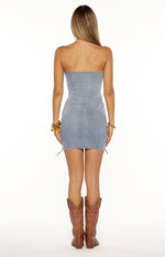 Rear view of a light wash denim strapless mini dress with a raw edge hem and side lace-up details