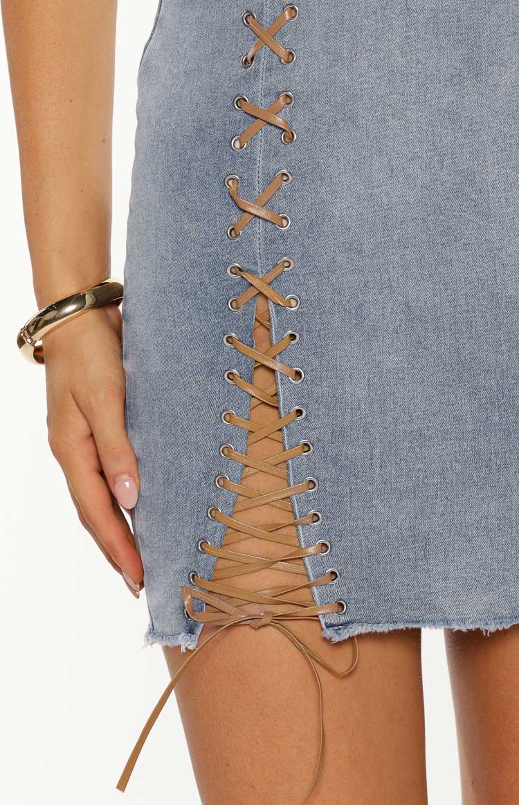 Close-up of the side lace-up detail on a light wash denim mini dress with tan lacing and silver eyelets