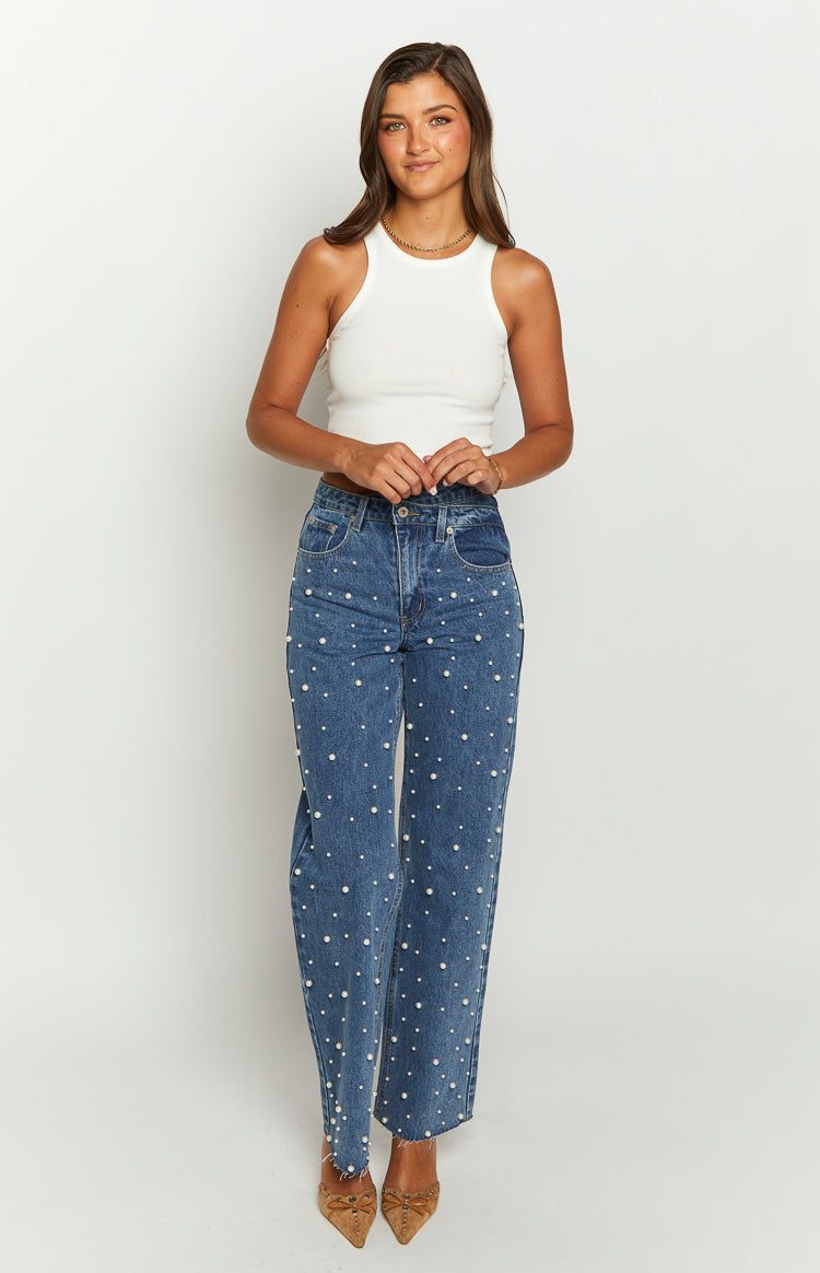 Front view of mid-wash blue high-waisted jeans with all-over pearl embellishments and a raw frayed hem