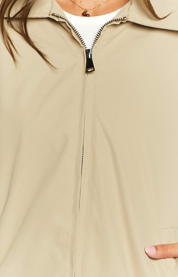 Close-up of the fawn windbreaker bomber jacket showing the partially unzipped black zipper and pointed collar