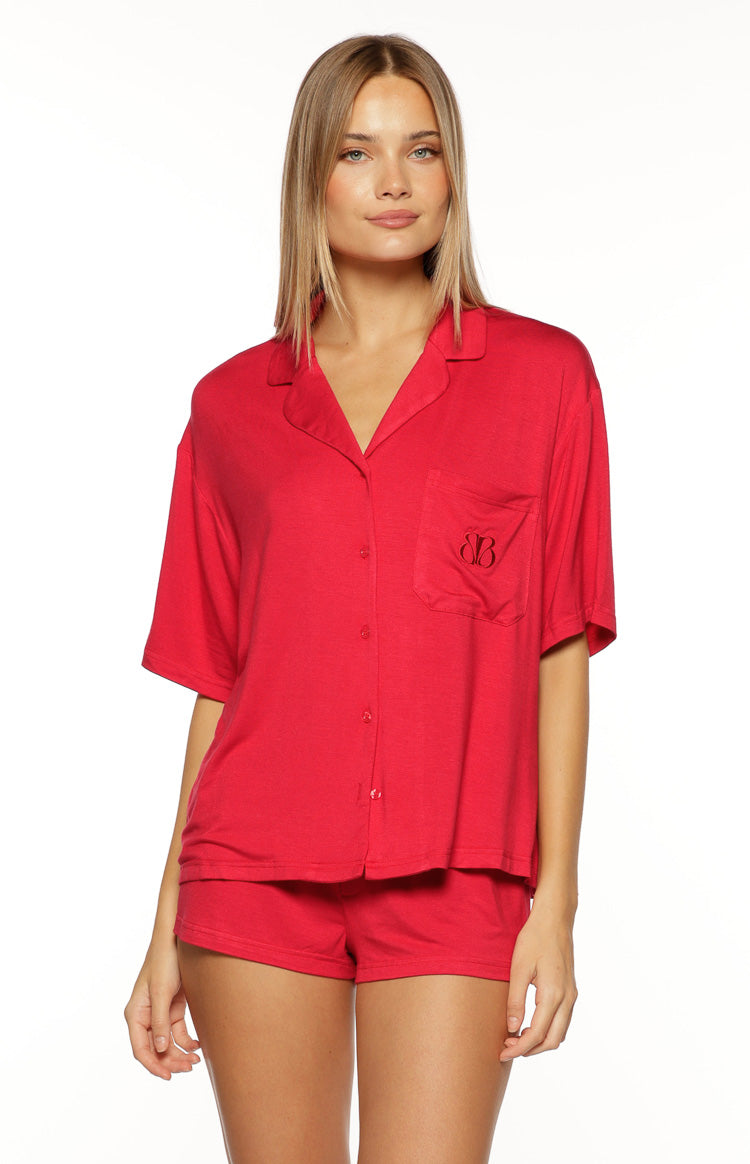 Front view of a red pajama shirt with a notched collar, V-neckline, short sleeves, and a button-front with an embroidered logo on the chest pocket