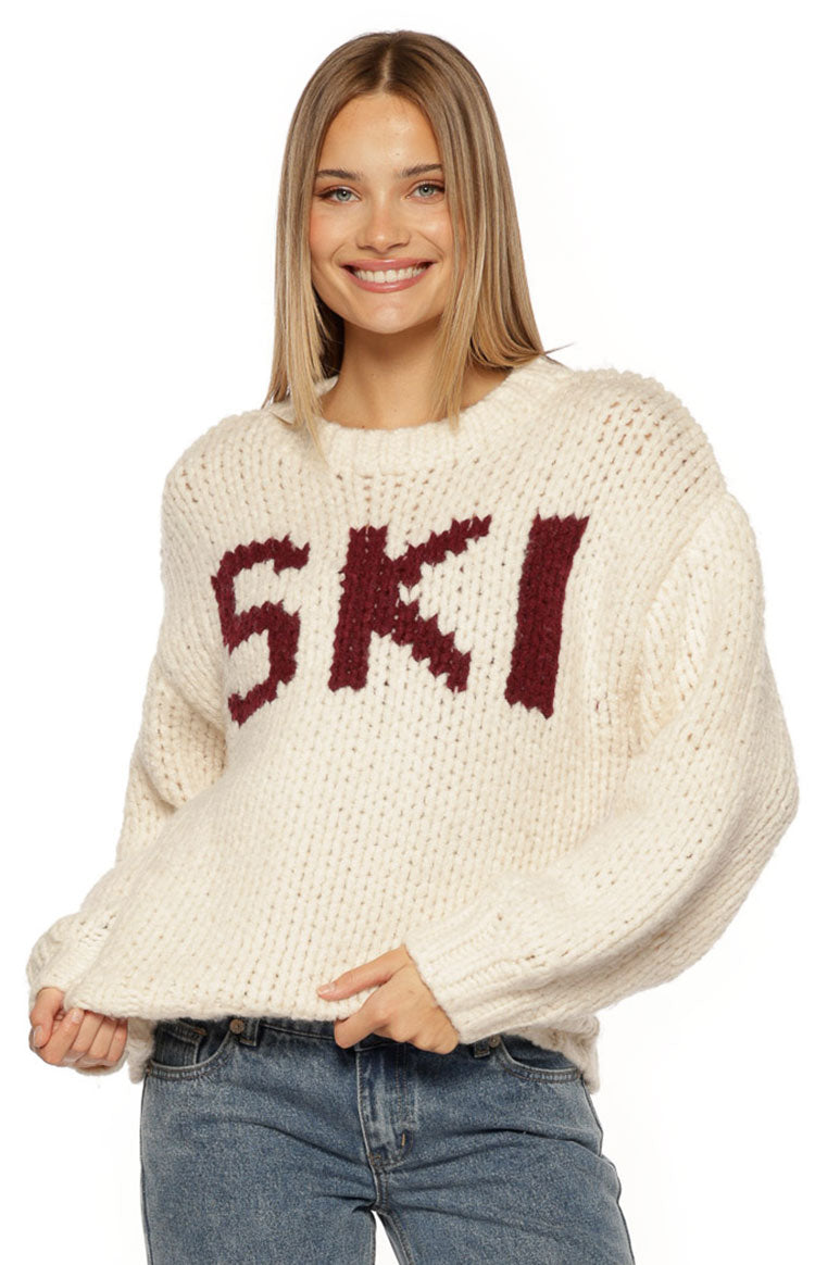 Front view of a cream chunky knit sweater with burgundy "SKI" jacquard lettering and ribbed cuffs