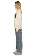 Side view of a cream chunky knit sweater with a relaxed fit and long sleeves, showing the burgundy jacquard pattern
