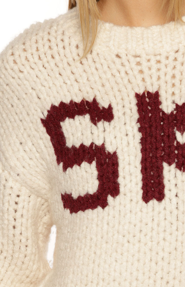 Close-up of the cream chunky knit sweater showing the dark red jacquard letter S