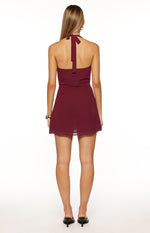 Rear view of a burgundy halter neck mini dress with a tie closure at the back of the neck and a flowy skirt