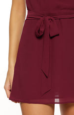 Close-up of the tied waist sash on a burgundy mini dress with a subtle sheer hem