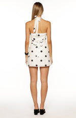Rear view of a white polka dot mini dress with a halter neck tie and a waist tie-back detail