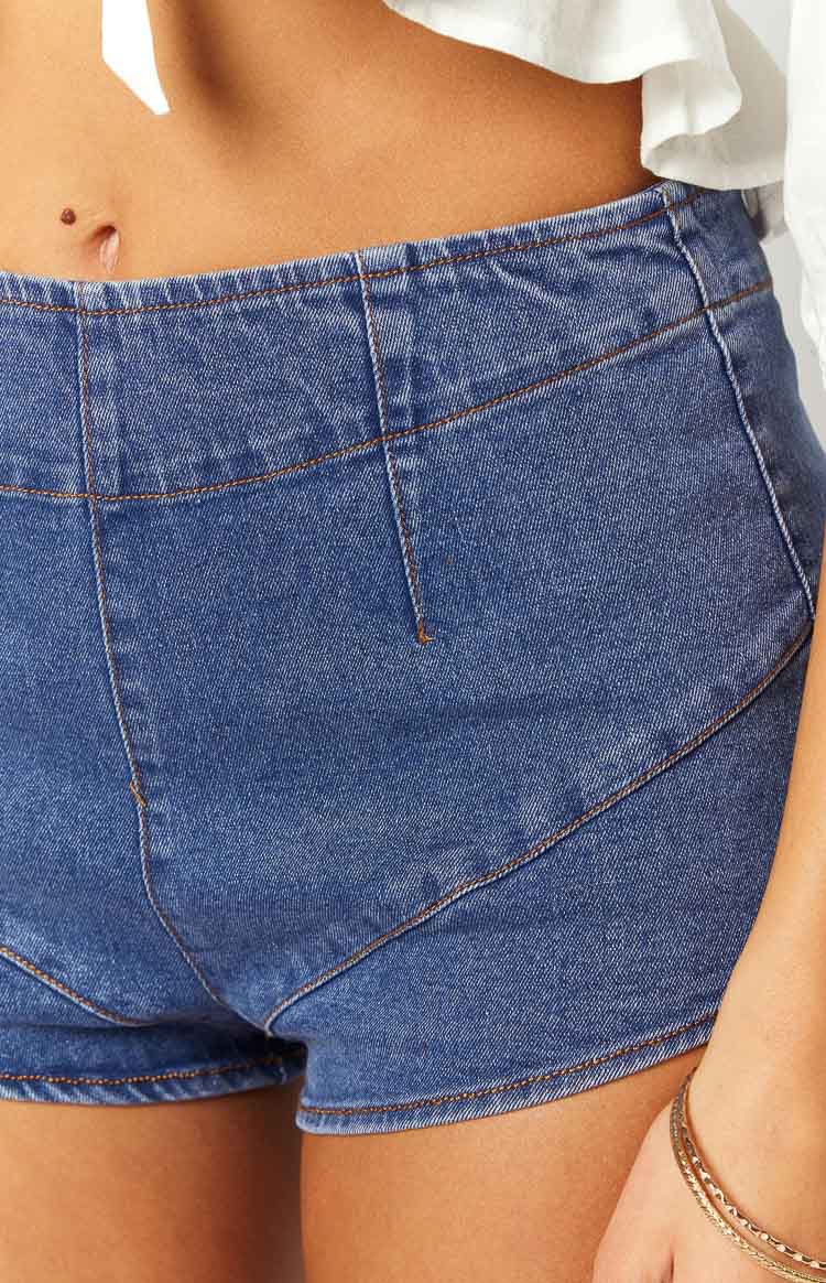 Close-up of the dark denim micro shorts showing the wide waistband and angled front seam details