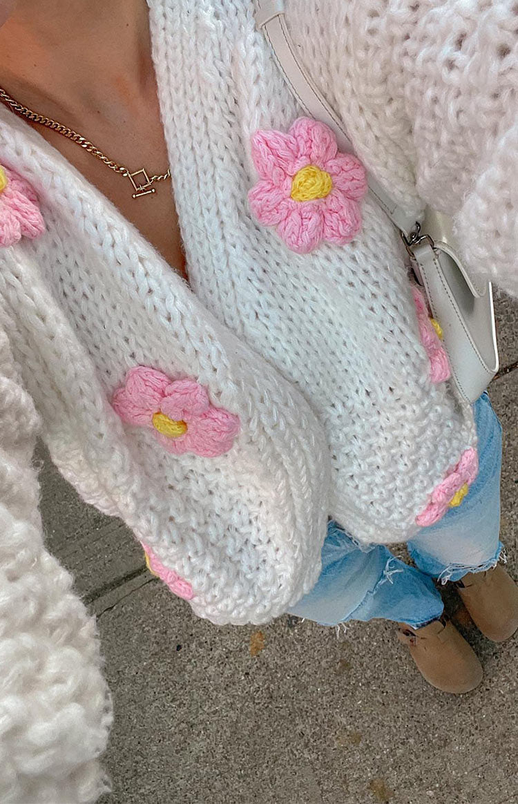 Close-up of the chunky white open knit cardigan with pink and yellow flower appliques on the sleeves