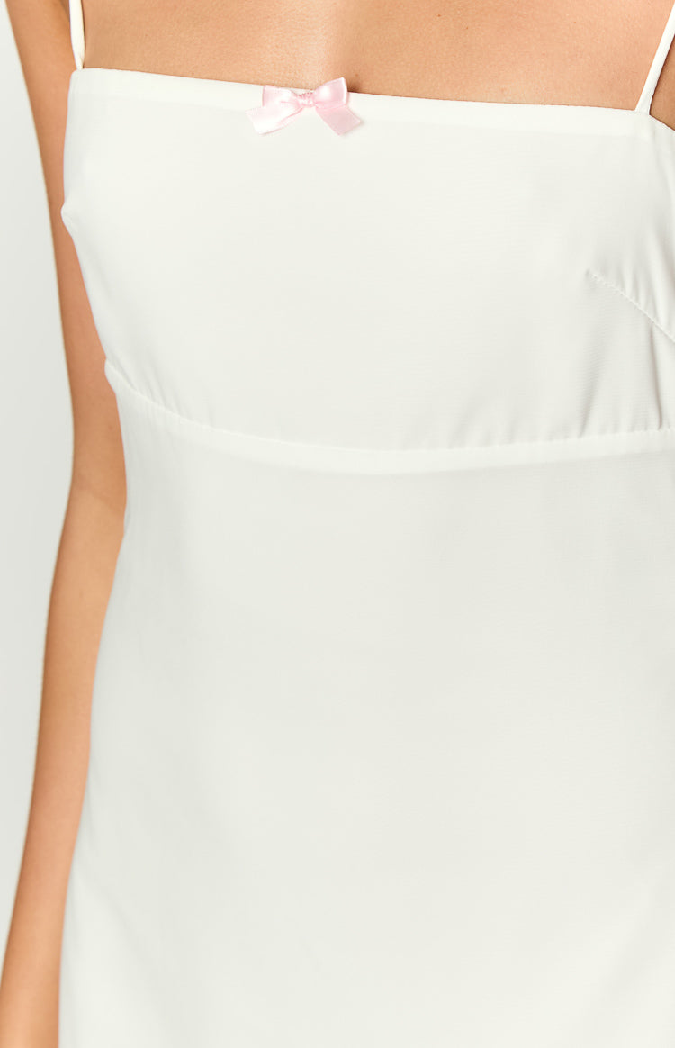 Close-up of the white mini dress showing a small pink bow detail and empire waist seam