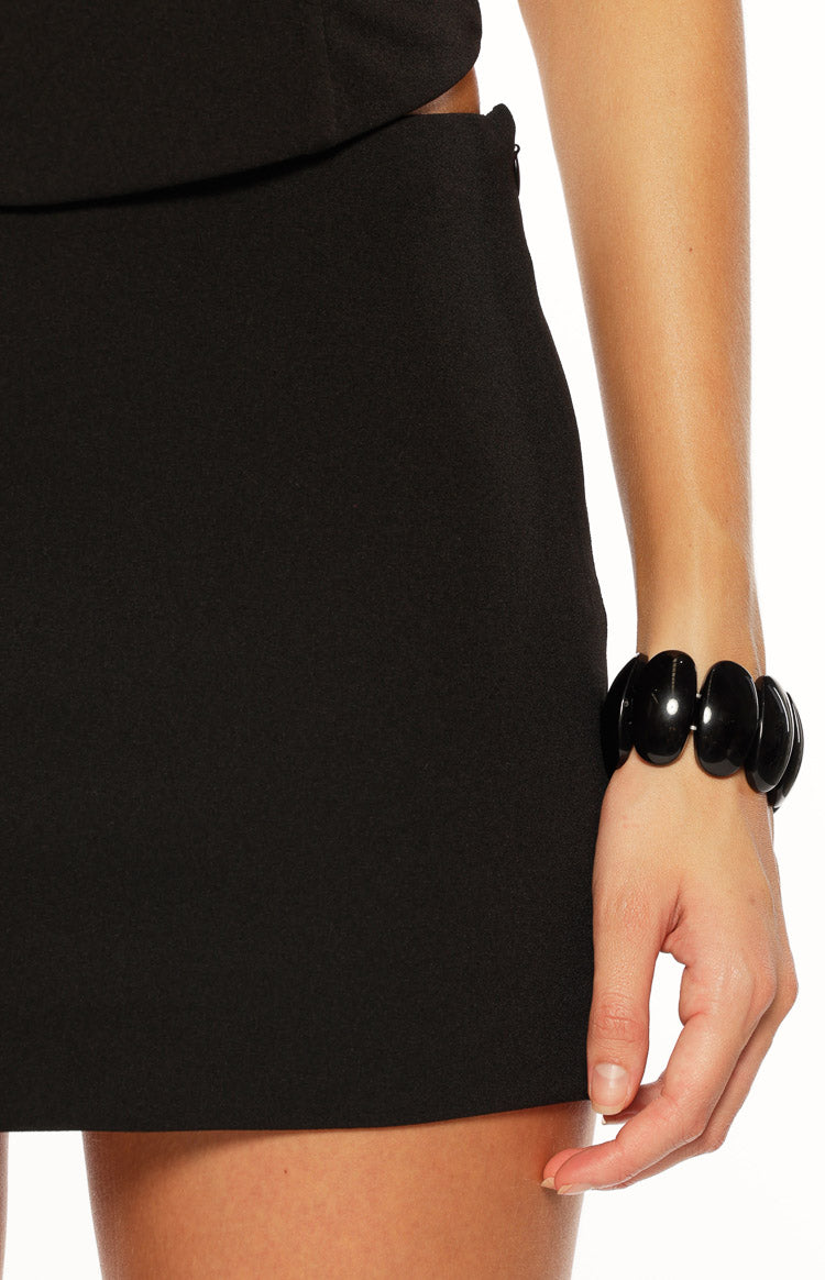 Close-up of the black mini skirt's side, showing the subtle zipper closure and smooth fabric
