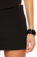 Close-up of the black mini skirt's side, showing the subtle zipper closure and smooth fabric