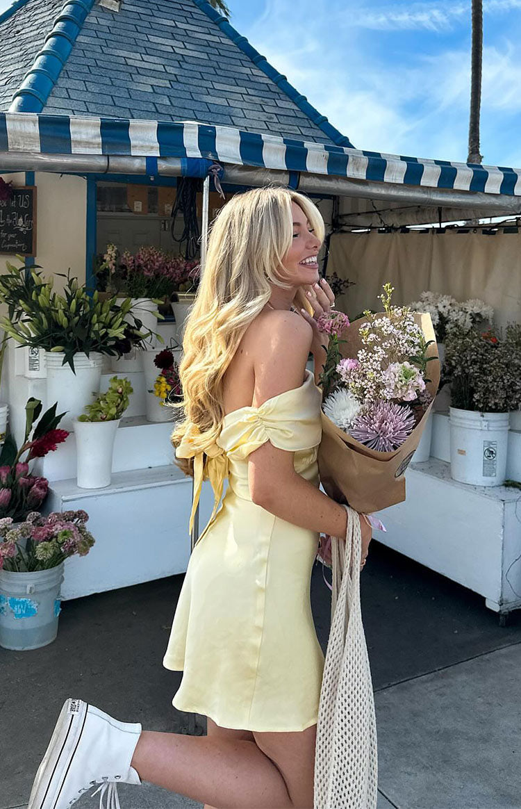 Side view of a primrose yellow satin mini dress with ruched off-shoulder sleeves and a tie-back
