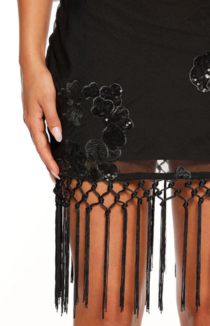 Close-up of the black sequin floral embroidery and macrame tassel fringe hem of a black mini dress