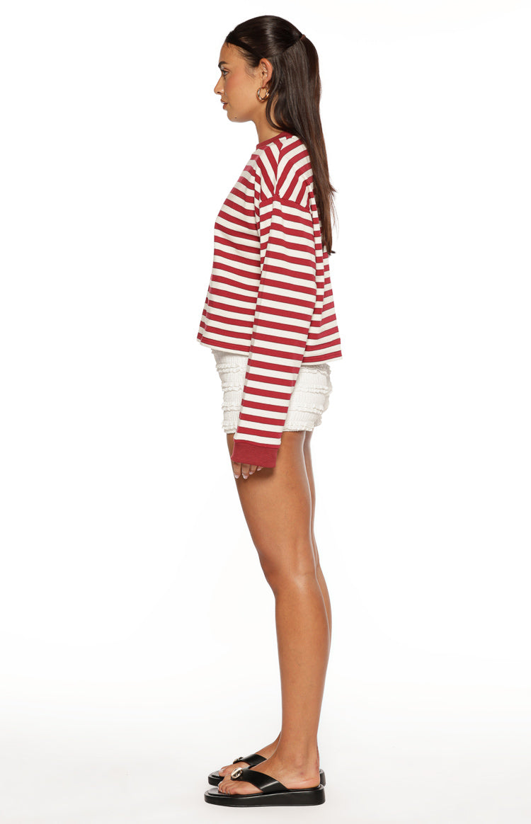 Side view of a relaxed fit burgundy and white striped long sleeve top with dropped shoulders and ribbed cuffs