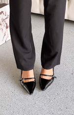 Close-up top view of black patent heels featuring a pointed toe and a delicate strap with a buckle