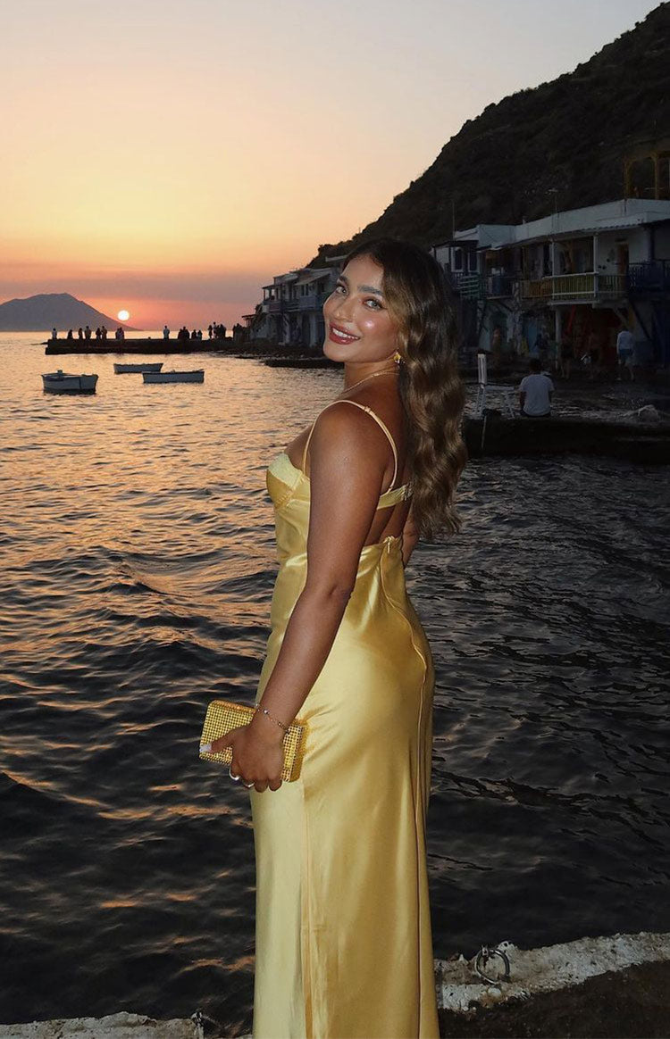 Side view of a yellow satin midi dress with a low scoop back, thin spaghetti straps, and a side leg slit