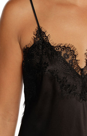 An extreme close-up of a black satin camisole highlighting the delicate black lace trim with fringed edges on the V-neckline and the thin spaghetti strap.