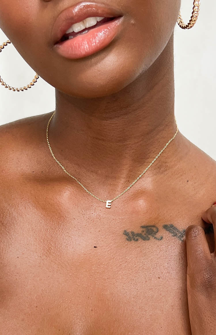Close-up showing the small gold letter E pendant on a delicate link chain necklace