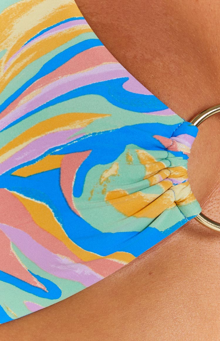 Close-up of the multi-coloured abstract print fabric with blue, green, pink, yellow, orange, and purple tones, ruched into a gold O-ring