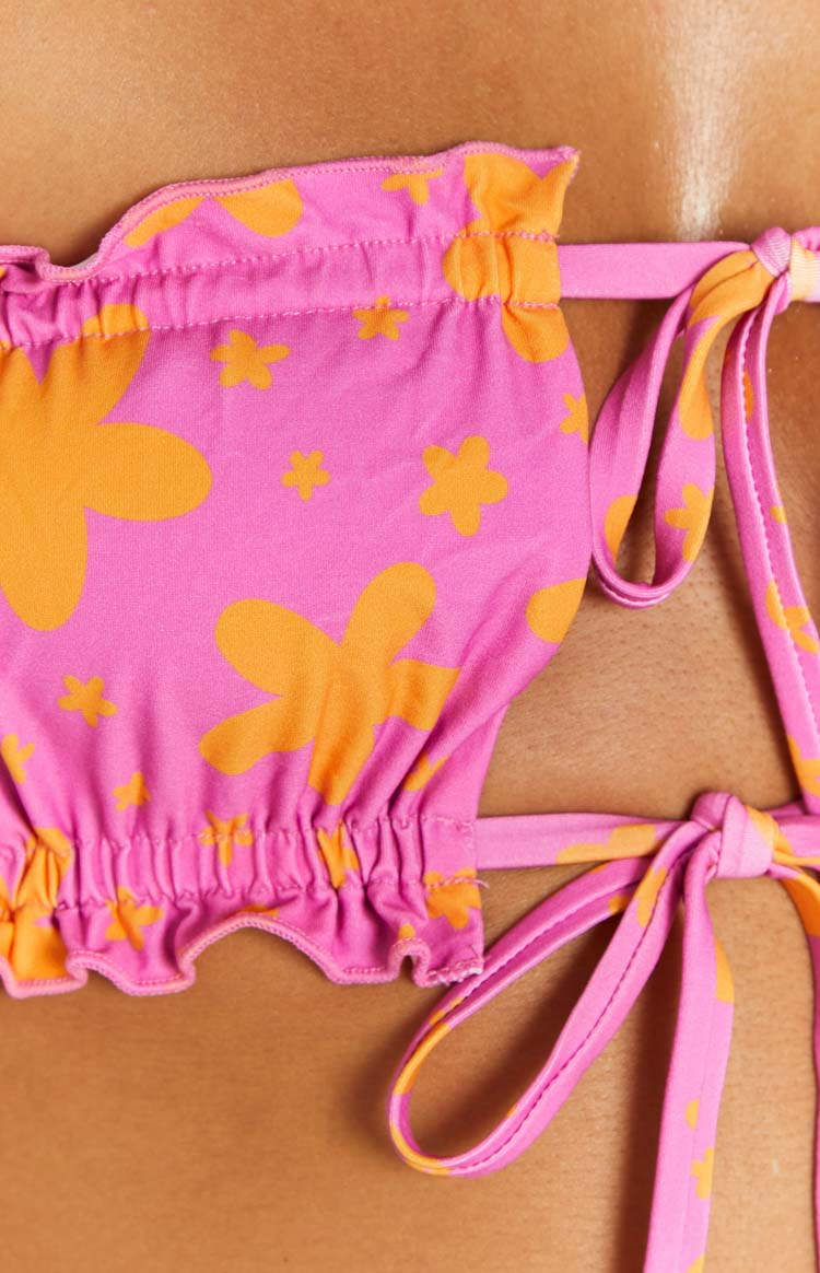 Close-up of the ruffled elasticated edges and side tie straps of a pink bikini top with orange floral print